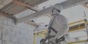 Construction worker in full protective gear, including helmet, mask, and gloves, standing on yellow scaffolding inside a building under construction.