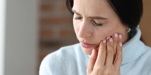 Woman with a pained expression, holding her jawline with her hand, indicating discomfort or tooth pain.