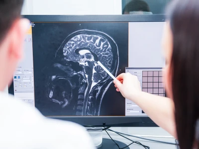 Medical professionals examine a brain MRI scan on a computer screen, with one person pointing at the image with a pen.