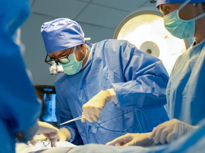 Surgeons in blue scrubs and masks perform an operation in a brightly lit operating room.