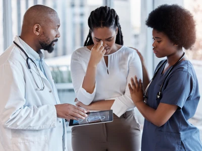 A doctor and two nurses are showing concern as they look at a tablet displaying a brain scan. One patient is holding her nose and appears distressed.