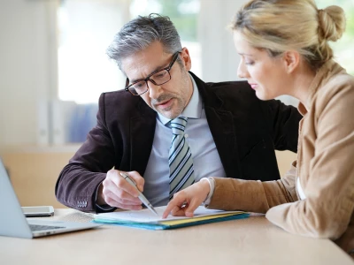 A man and woman are reviewing documents together at a desk, engaging in a discussion in a bright, modern office setting.