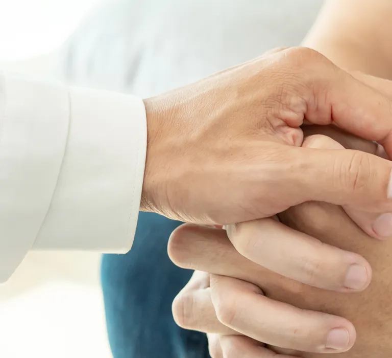 A healthcare professional's hand gently holds a patient's hand in a comforting gesture.