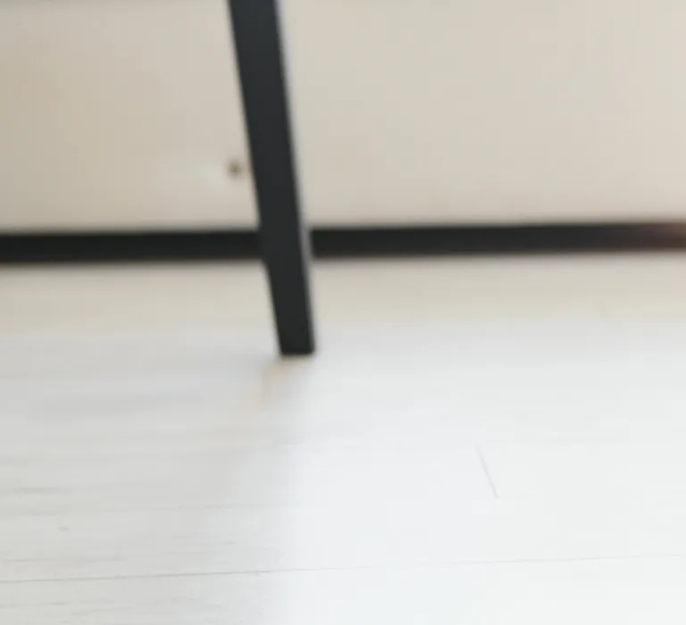 Person with a prosthetic leg tying shoelaces on a black sneaker. They are kneeling beside a white couch on a light-colored wooden floor.