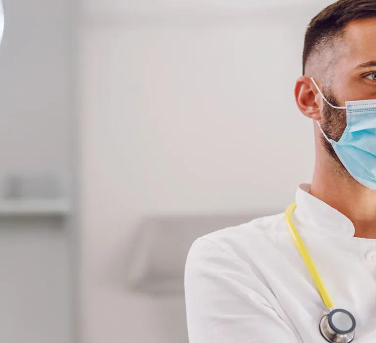 A male doctor wearing a face mask and stethoscope examines an X-ray in a medical facility.