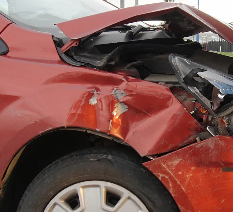 A red car with significant front-end damage collides with the front of a blue truck; the impact crushed the hood and front panel of the red vehicle.