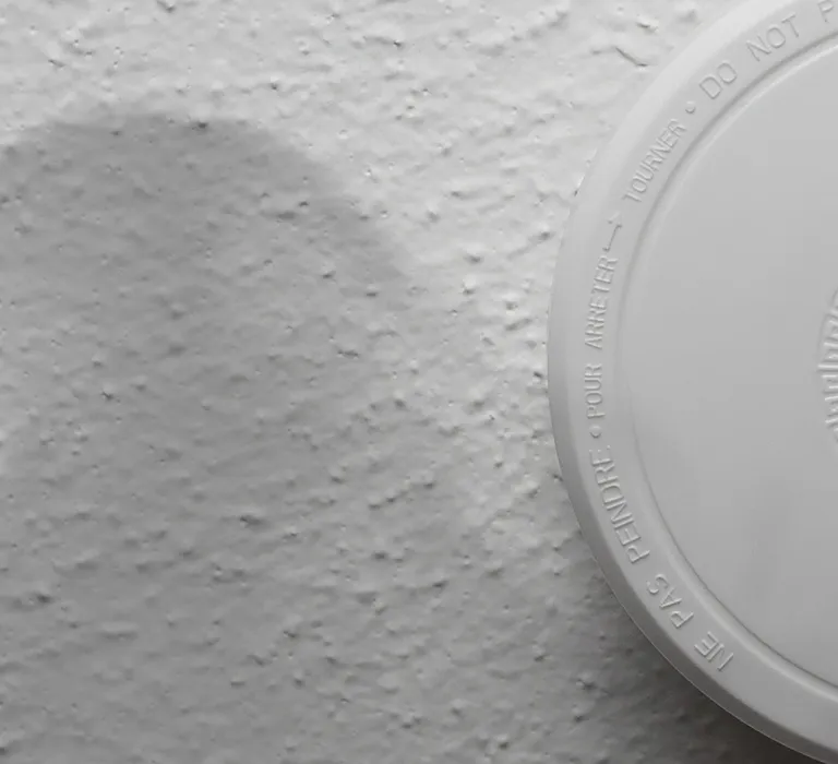 A smoke detector on a textured white ceiling with a red warning light illuminated.