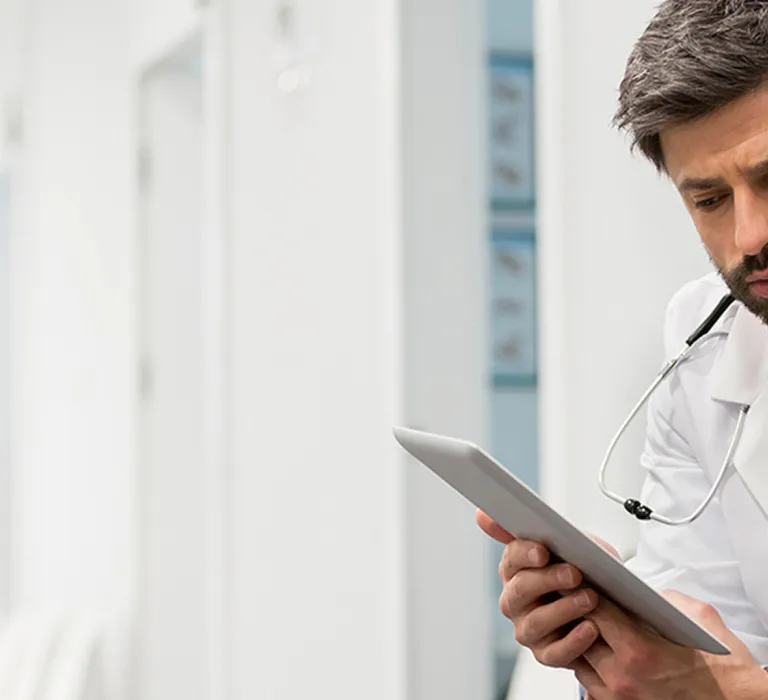 A doctor and a man are looking at a tablet together in a clinical setting, both appearing focused and concerned.